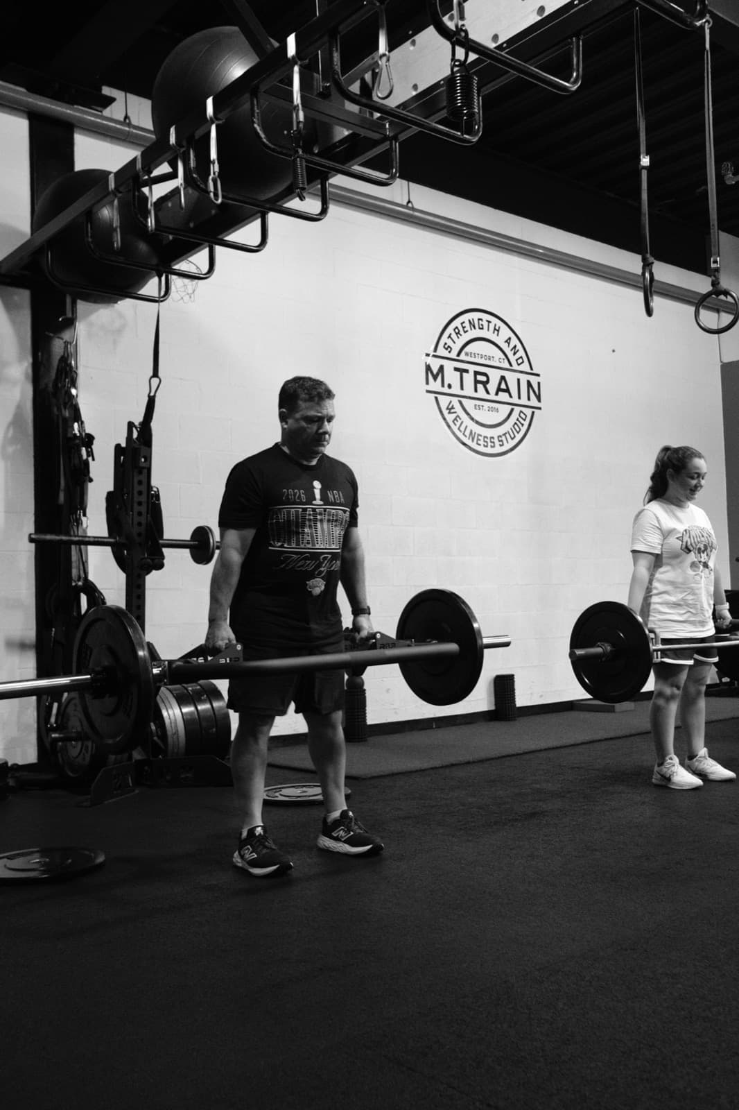 Trap-bar deadlift under the M.Train Strength and Wellness logo